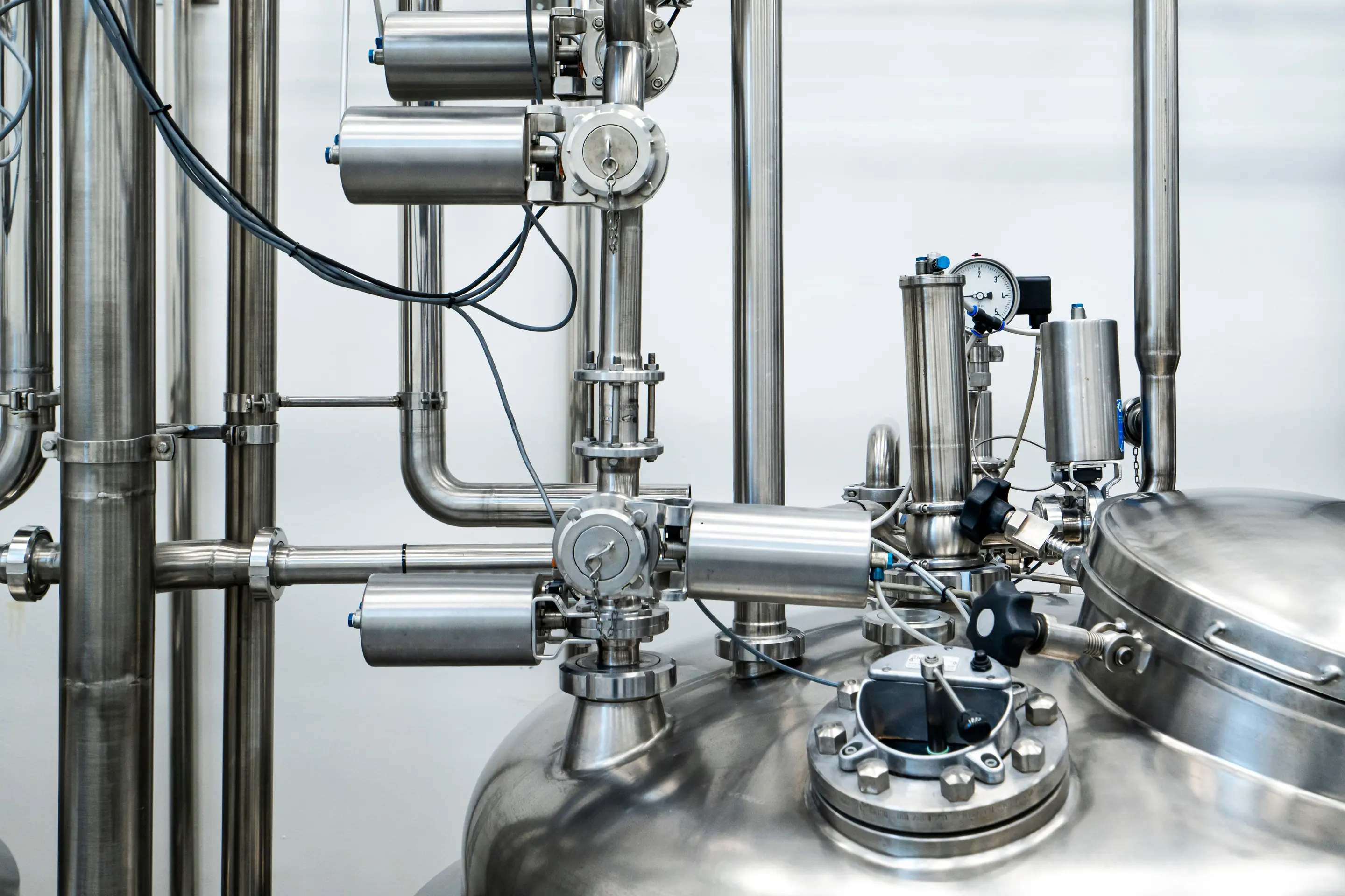 Stainless steel process equipment on top of a vessel: a pressure gauge, air-actuated valves and the manway.