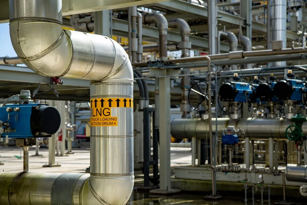 Insulated process piping with a printed line marker, actuated control valves, and a handwheel on a pipe rack.