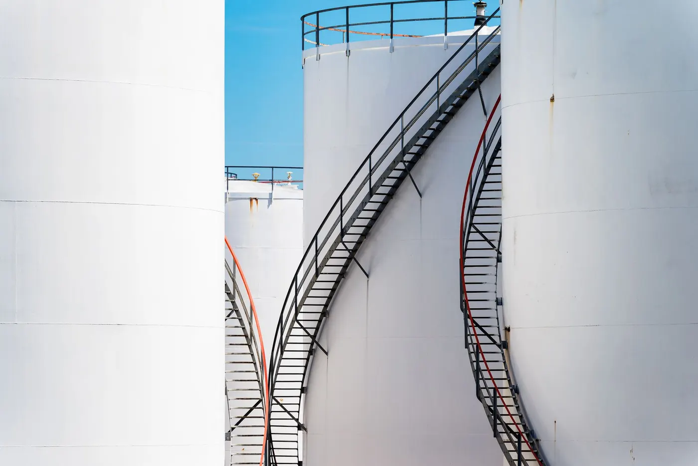 A spiral staircase on a white storage tank at an industrial plant.